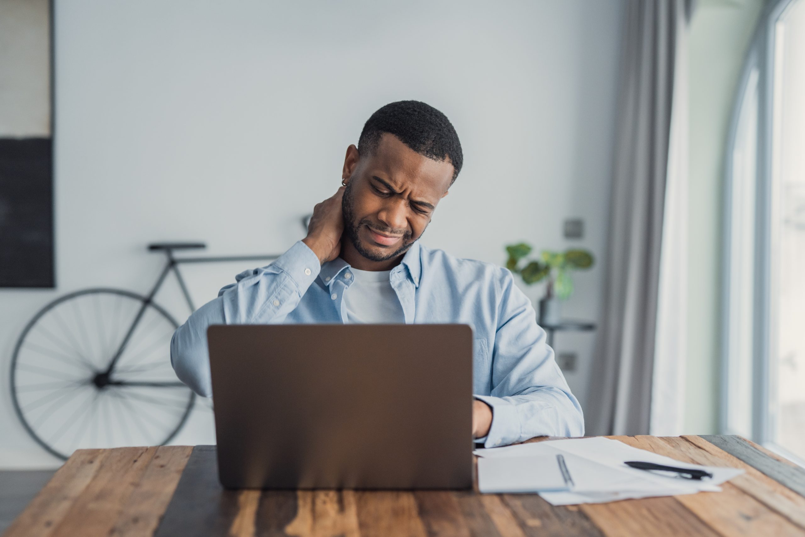 Man experiencing neck pain while working on a laptop at home.