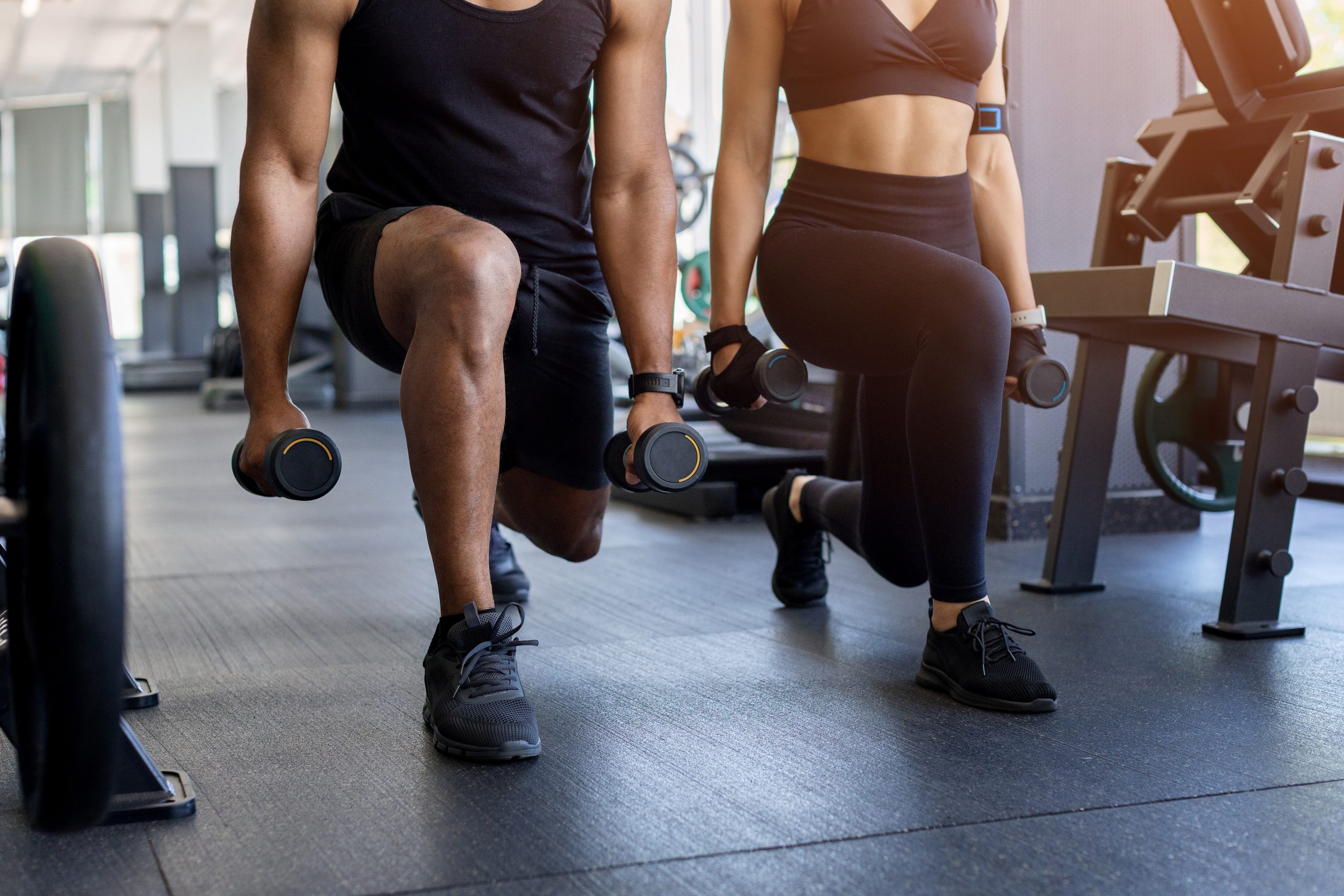 Man and woman performing weighted lunges during a gym workout.