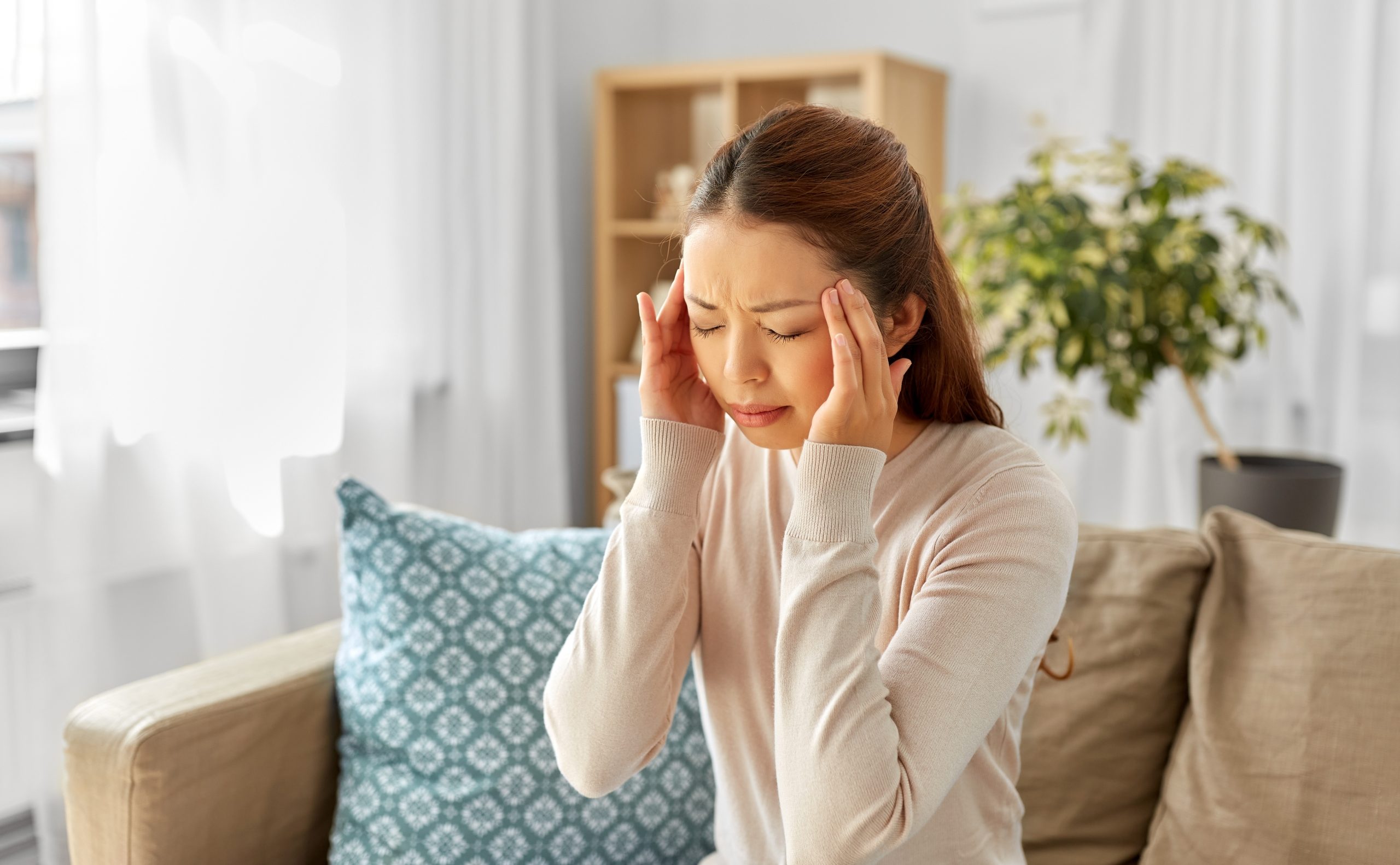 Woman holding her temples while experiencing a headache at home.