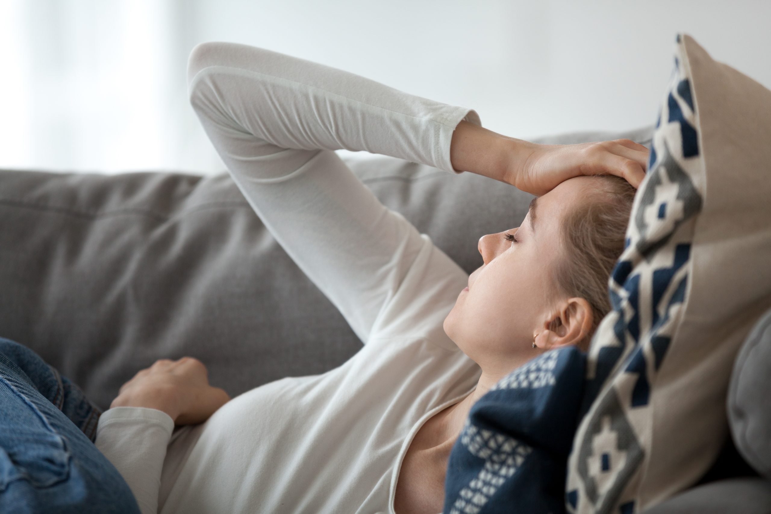 Woman resting on a couch while experiencing a migraine or severe headache.
